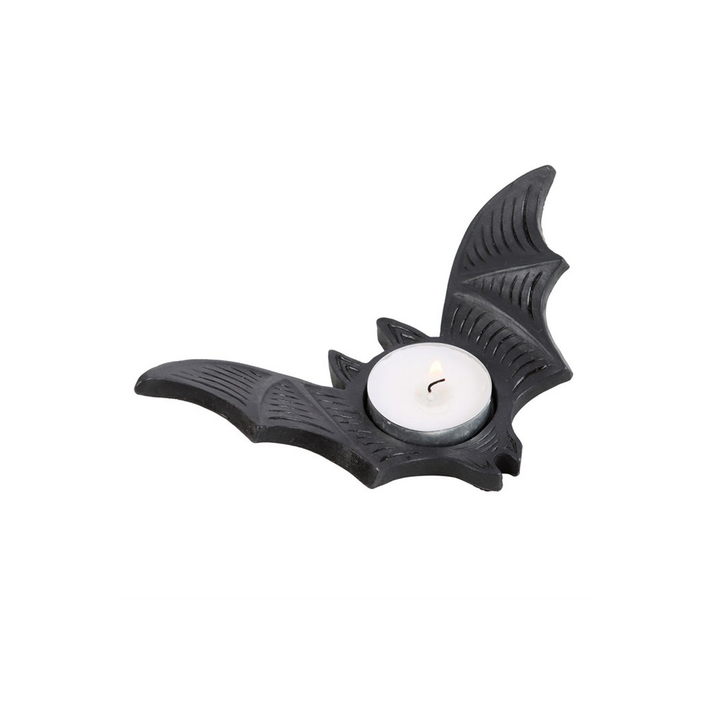 Black bat-shaped candle holder with a lit white candle on a white background