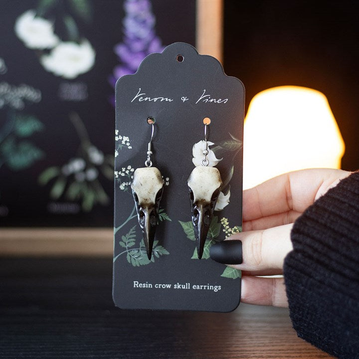 Resin crow skull earrings on a branded card held by a person.
