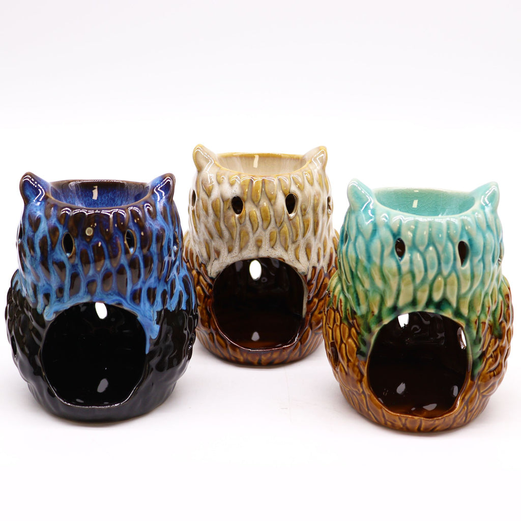 Three ceramic owl-shaped candle holders in blue, beige, and green on a white background