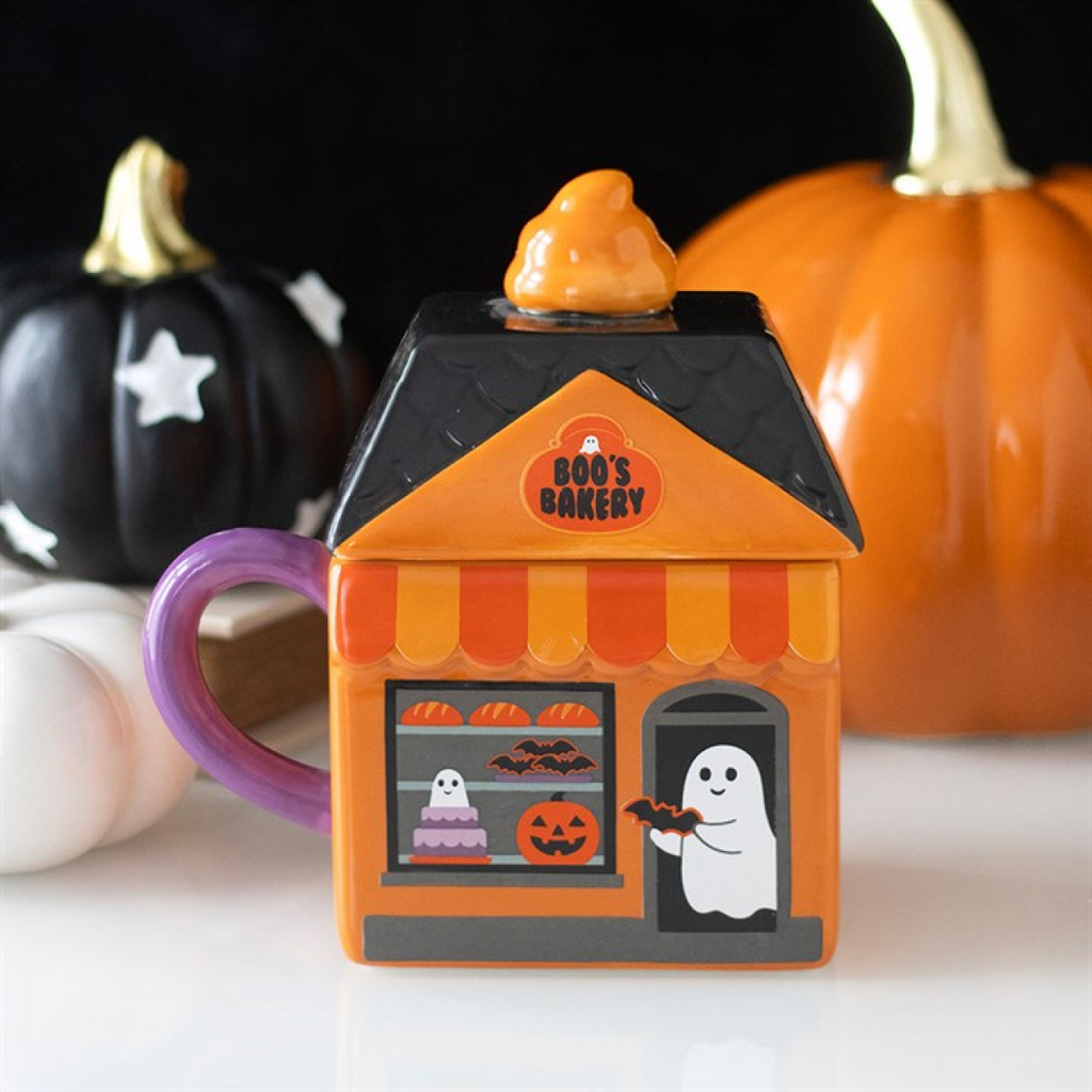 Halloween-themed mug shaped like a house with a ghost and pumpkins on a white surface.