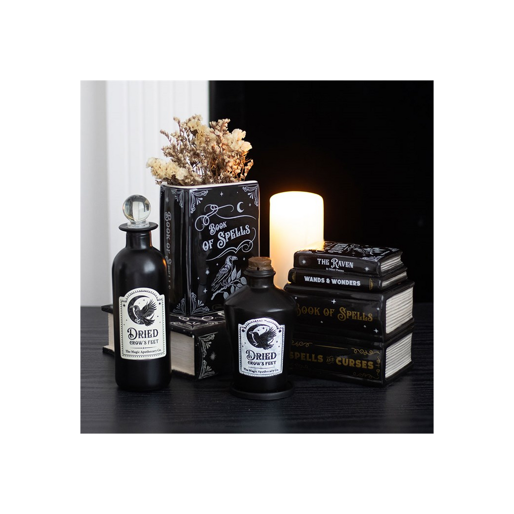 Decorative set with black bottles labeled 'Dried Gravestones' and 'Wards & Wonders', surrounded by books and a candle.