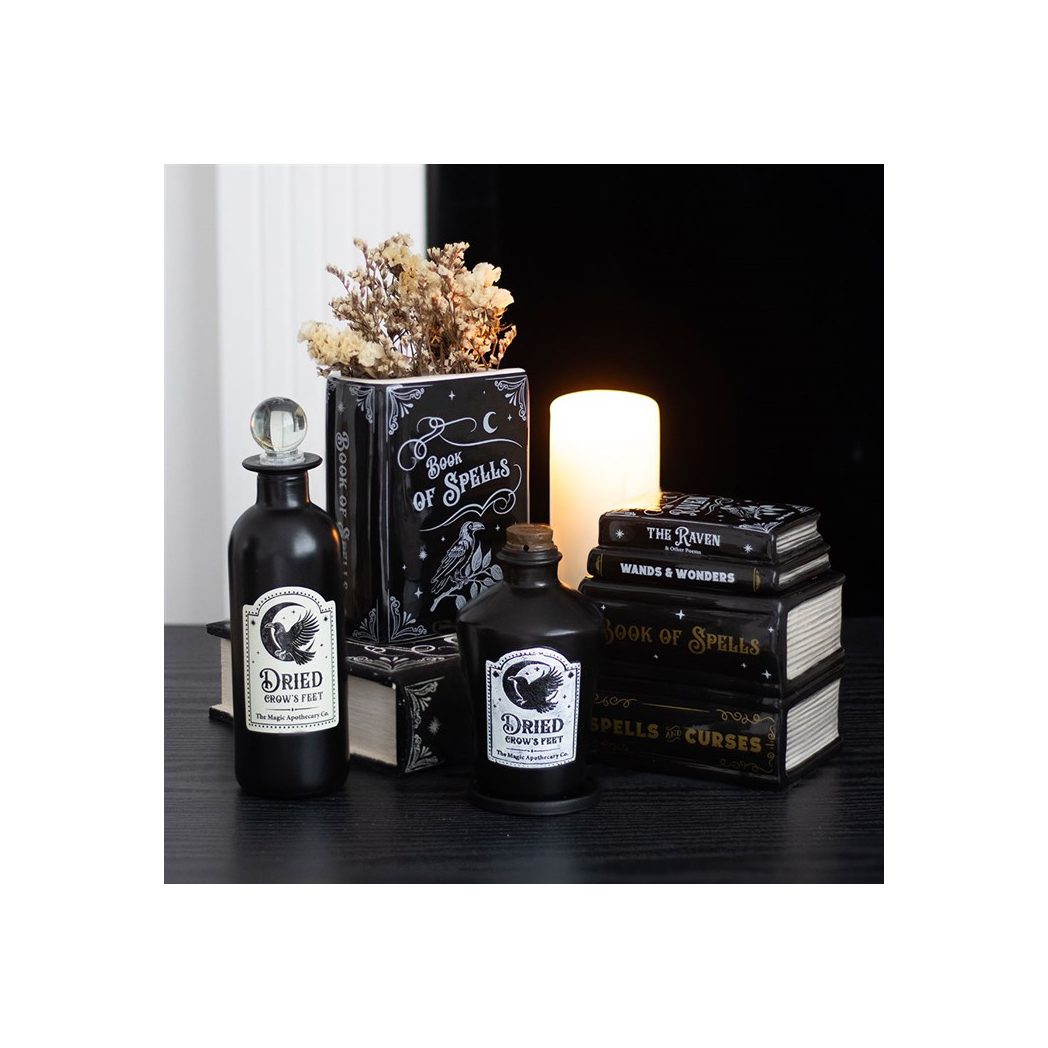 Decorative set with black bottles labeled 'Dried Gravestones' and 'Wards & Wonders', surrounded by books and a candle.