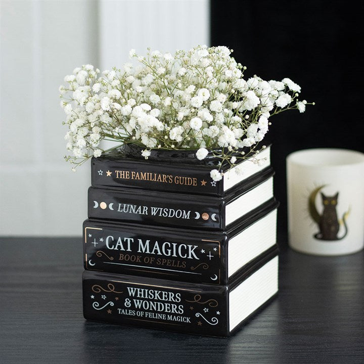 Stack of black books with gold text on a dark surface, topped with white flowers.
