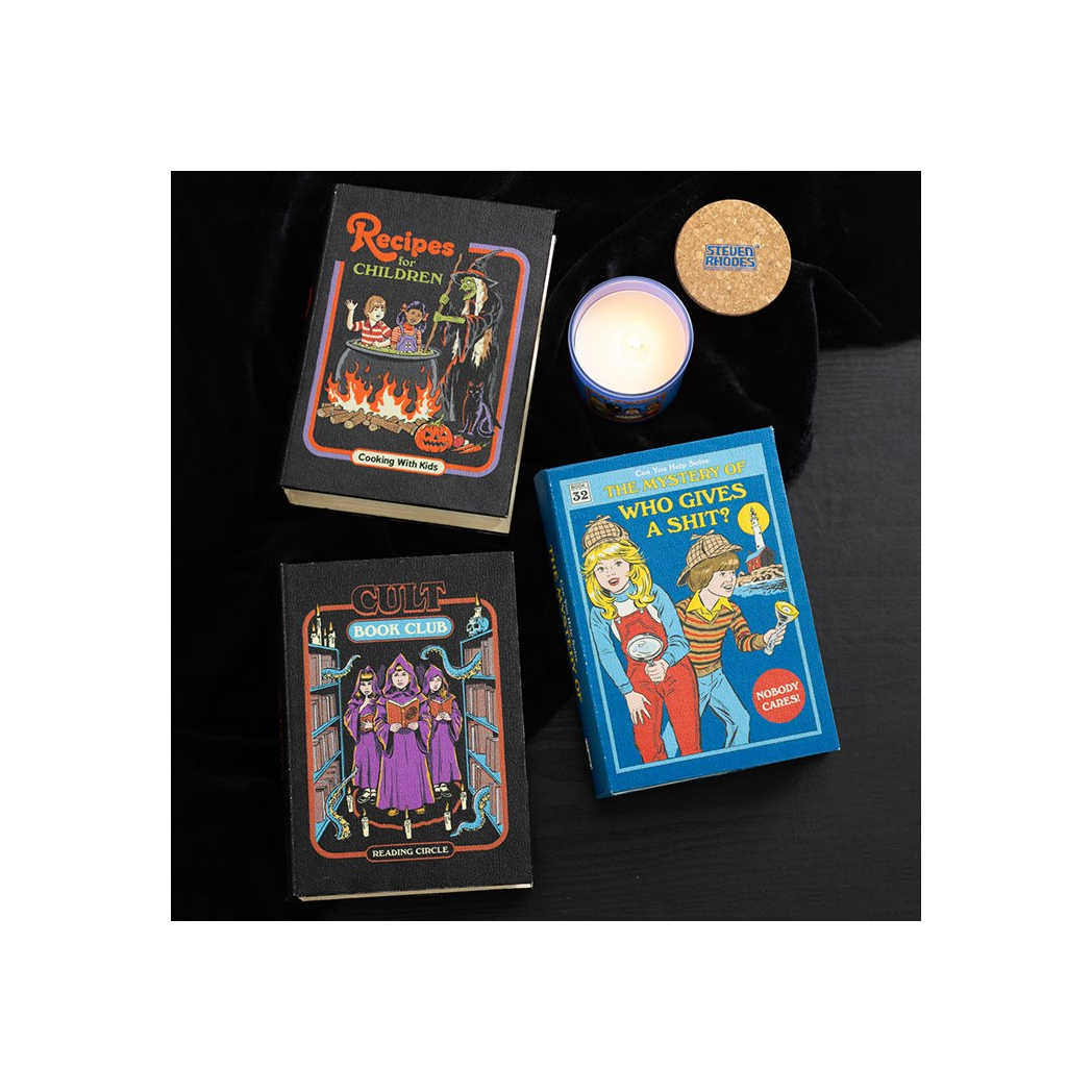 Three books with colorful covers on a dark surface, one of which is lit by a candle.