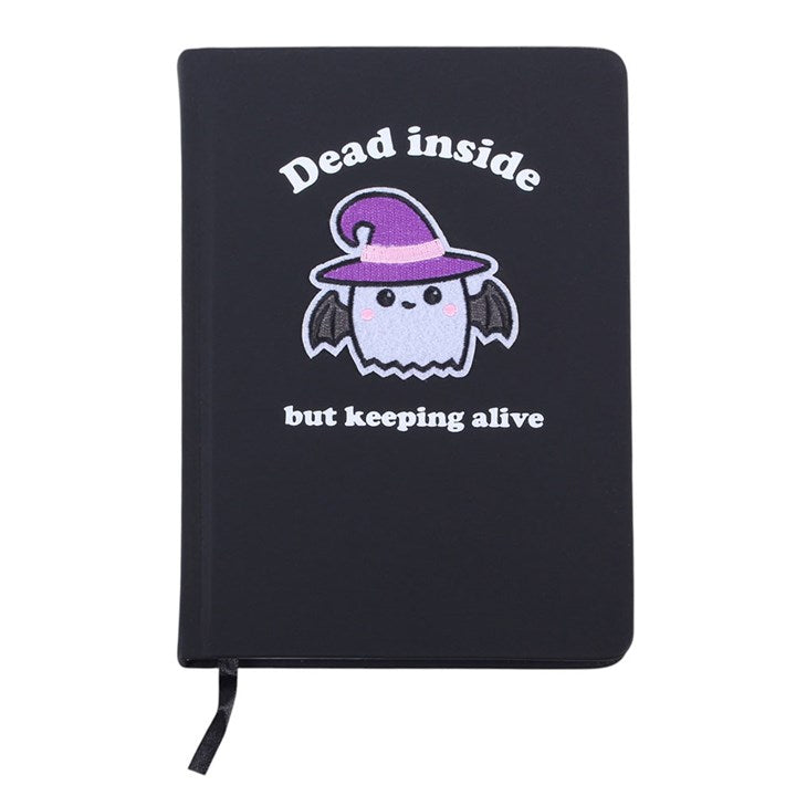 A black hardcover notebook with a black elastic bookmark ribbon, featuring a cute cartoon ghost wearing a purple witch hat with the text 'Dead inside but keeping alive' printed on the front, set against a plain white background.