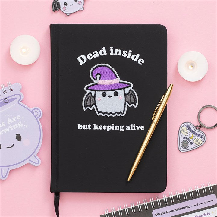 Black notebook with a cute ghost design and text on a pink background with decorative items.