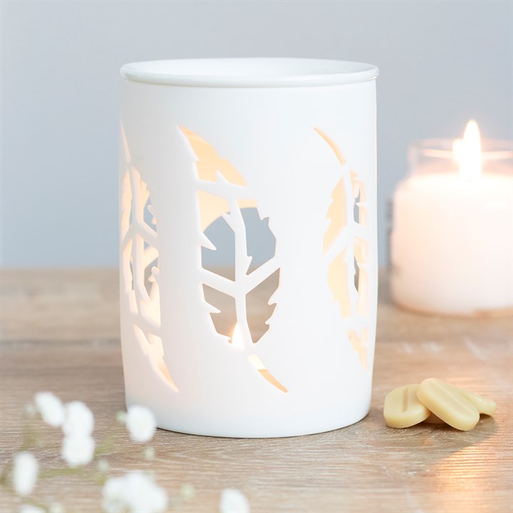 White candle holder with leaf cutouts on a wooden surface with a lit candle in the background.