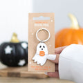 Halloween-themed ghost keychain on a cardboard backing with pumpkins in the background