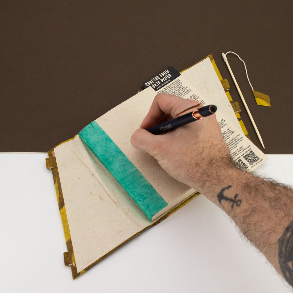 Hand writing in a notebook with a pen on a white surface.