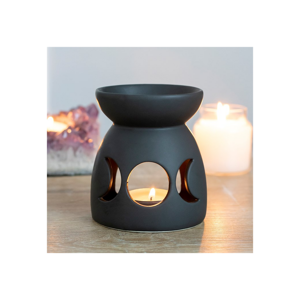 Black ceramic oil burner with cut-out moon phases on a wooden surface.