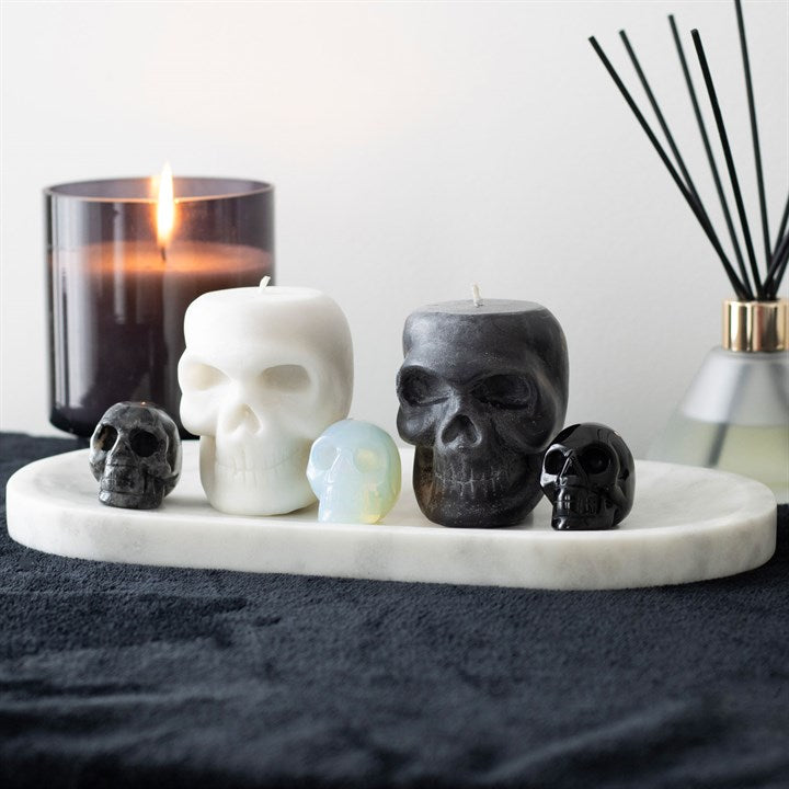 Skull-shaped candles on a marble tray with a lit candle in the background.