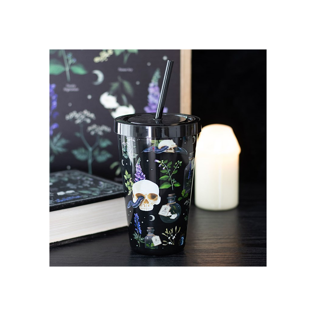 Tumbler with skull and potion design on a dark surface with a candle and book in the background