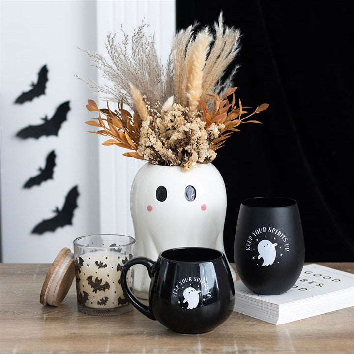 Halloween-themed decor with a vase, mugs, and candles on a table.