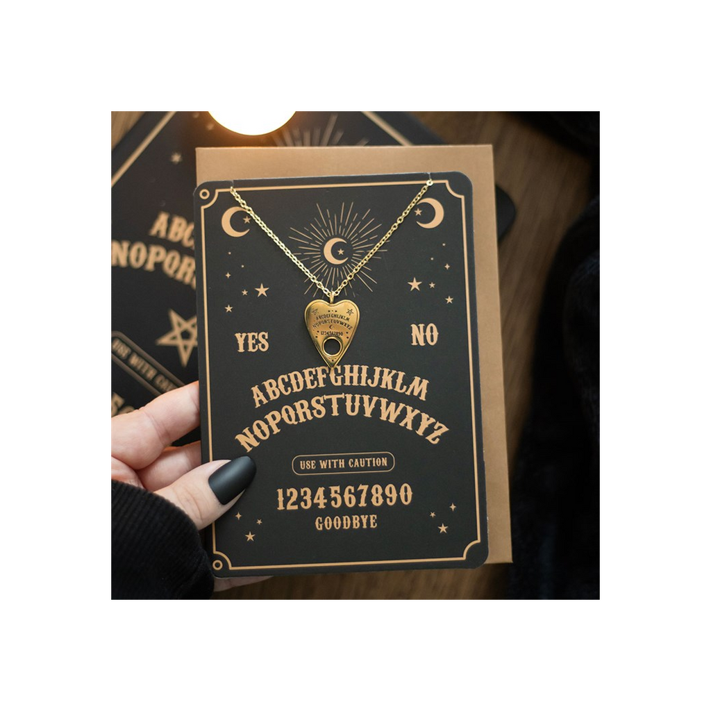 Heart-shaped pendant necklace on a card with Ouija board text, held by a hand.