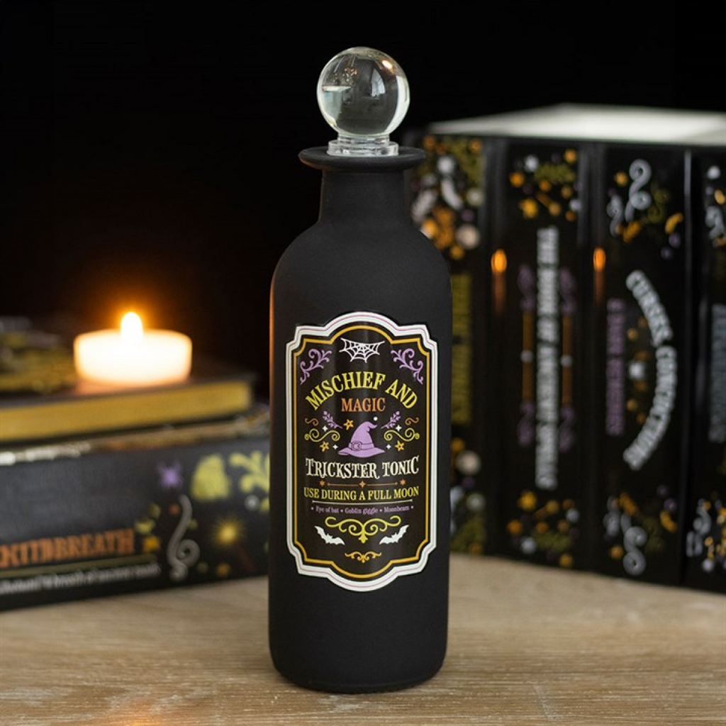 Black bottle labeled 'Mischief and Magic Trickster Tonic' with a candle and books in the background.