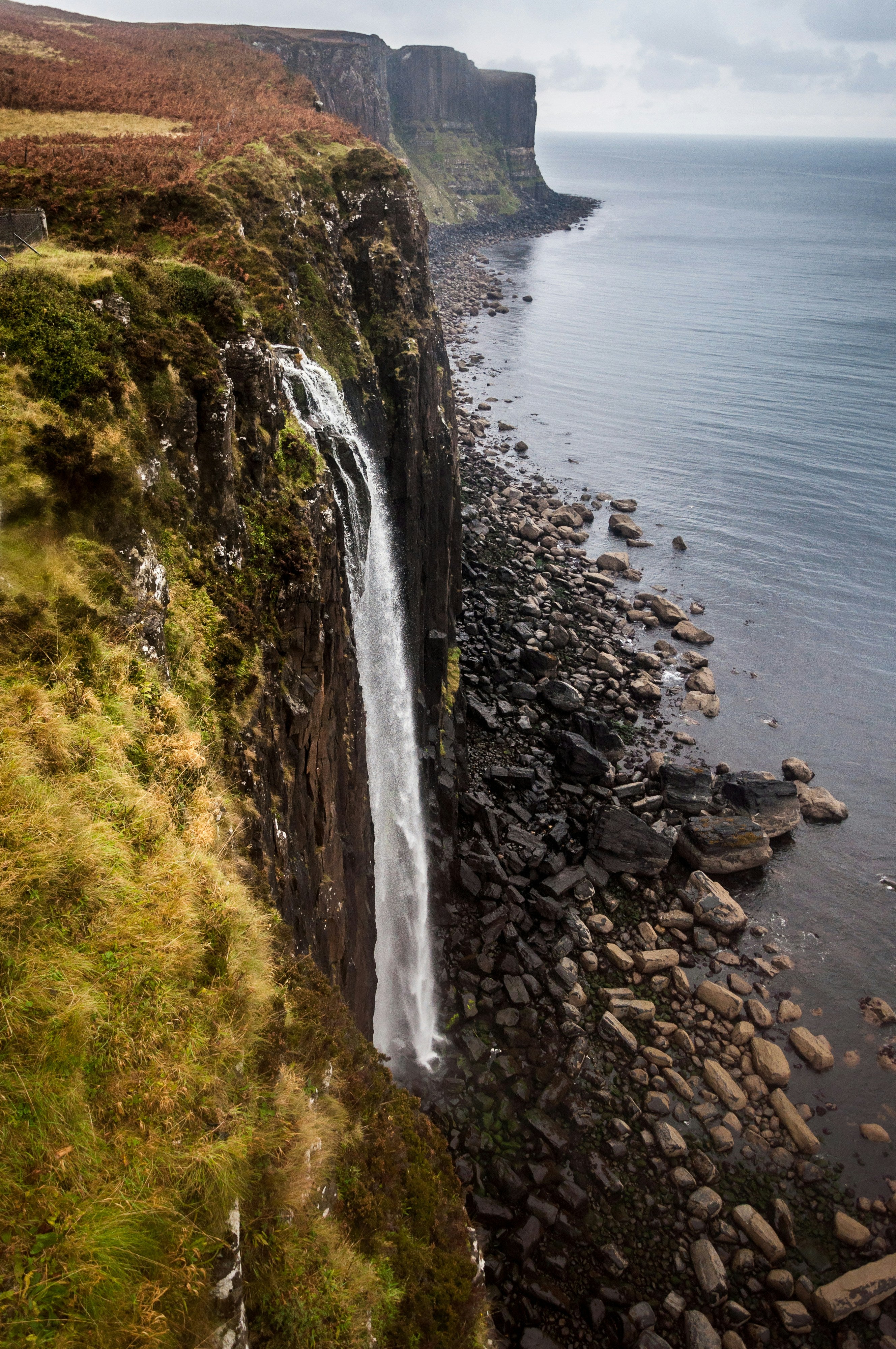 Waterfall cascading down a cliff into the ocean with a rocky shoreline.