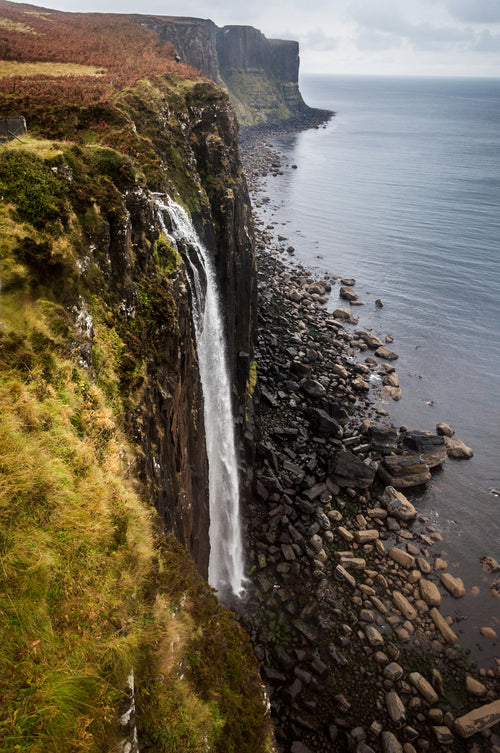 Waterfall cascading down a cliff into the ocean with a rocky shoreline.