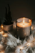 Candle burning on a fur surface with decorative lights and a plant in the background